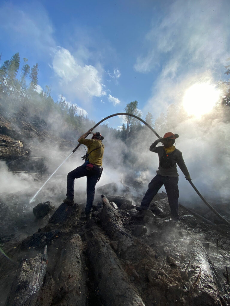Two wildland firefighters in action with a hose on a sunny day